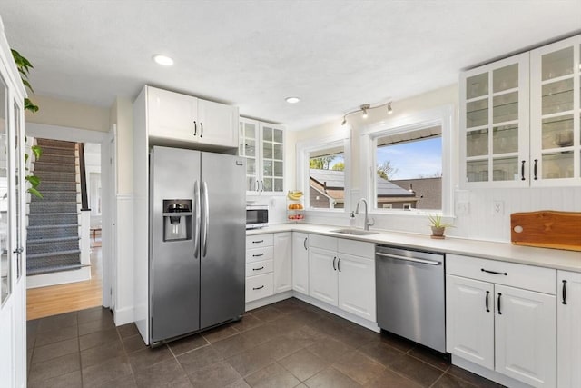 kitchen featuring white cabinets, appliances with stainless steel finishes, glass insert cabinets, and a sink