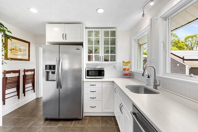 kitchen with white cabinets, appliances with stainless steel finishes, a sink, light countertops, and glass insert cabinets