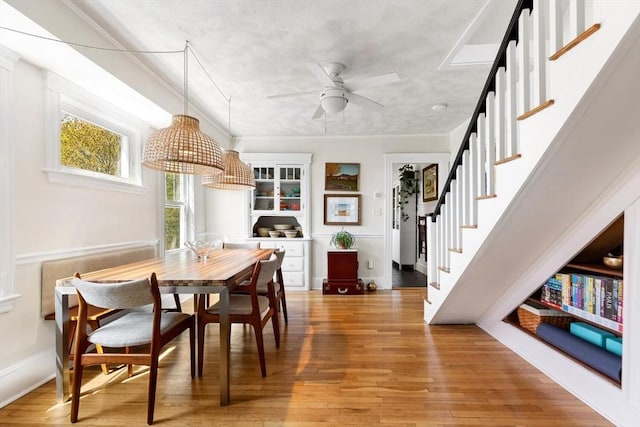 dining space with a ceiling fan, baseboards, stairway, and light wood-type flooring