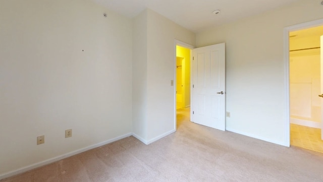 unfurnished bedroom featuring ensuite bath, a walk in closet, and light colored carpet