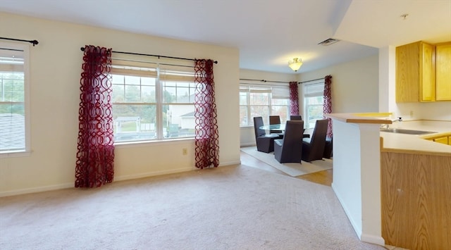 kitchen featuring kitchen peninsula, light brown cabinets, light colored carpet, and sink