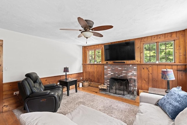 553 Center St, Hanover, MA 02339 - living room featuring wooden walls, wood finished floors, a ceiling fan, a fireplace, and a wainscoted wall