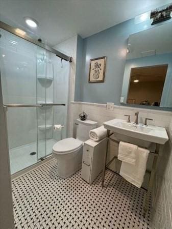 bathroom featuring vanity, toilet, a shower with door, and tile walls