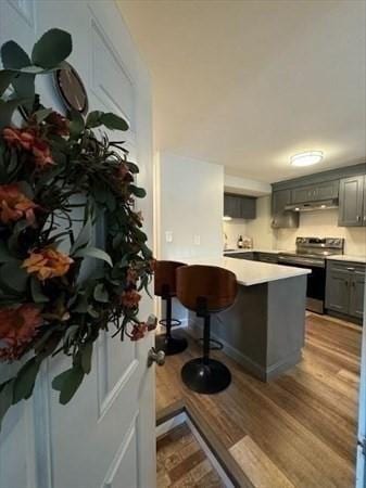 kitchen featuring gray cabinetry, kitchen peninsula, a kitchen bar, electric stove, and light wood-type flooring