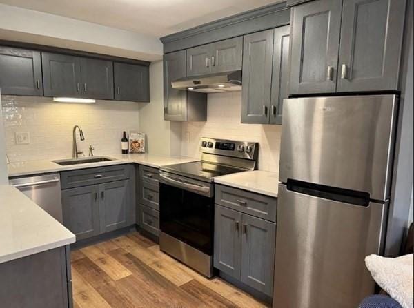 kitchen featuring backsplash, sink, gray cabinets, light wood-type flooring, and stainless steel appliances