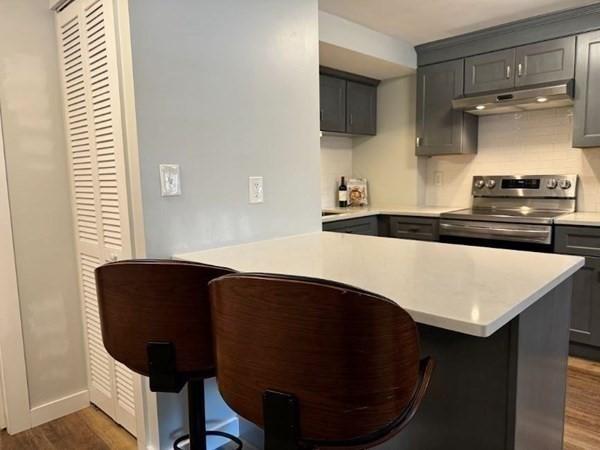 kitchen with gray cabinetry, dark hardwood / wood-style flooring, stainless steel range with electric cooktop, and a breakfast bar