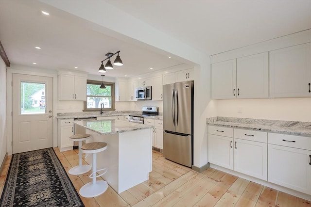 649 S Main St, Raynham, MA 02767 - kitchen featuring stainless steel appliances, white cabinetry, light wood-style flooring, a center island, and light stone countertops