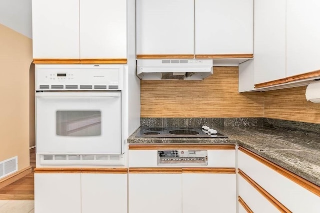 kitchen with dark stone countertops, white oven, white cabinets, and electric stovetop