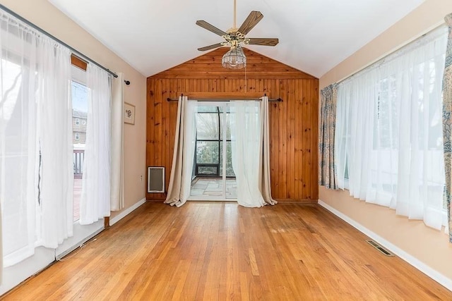 unfurnished room featuring lofted ceiling, a healthy amount of sunlight, and wood walls