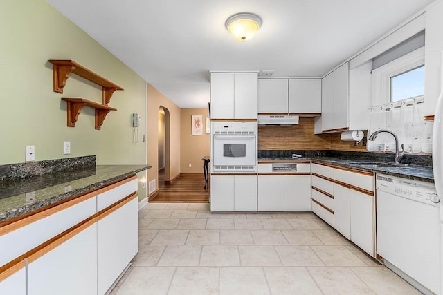 kitchen featuring backsplash, sink, white appliances, white cabinets, and dark stone counters