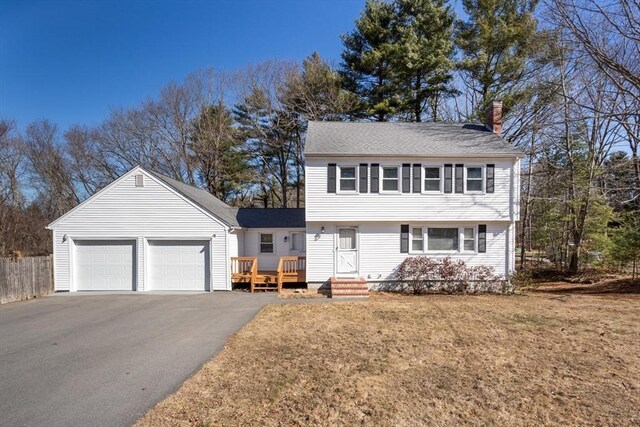 colonial home with a front lawn, a garage, driveway, and a chimney
