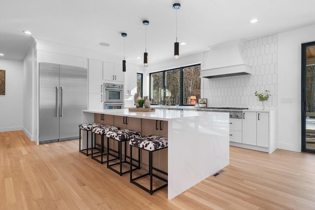 kitchen with white cabinetry, a center island, hanging light fixtures, custom range hood, and stainless steel appliances