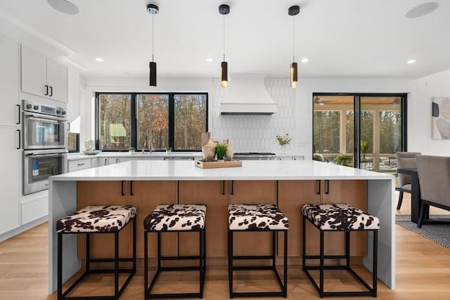 kitchen featuring stainless steel double oven, a kitchen island, custom exhaust hood, and white cabinets