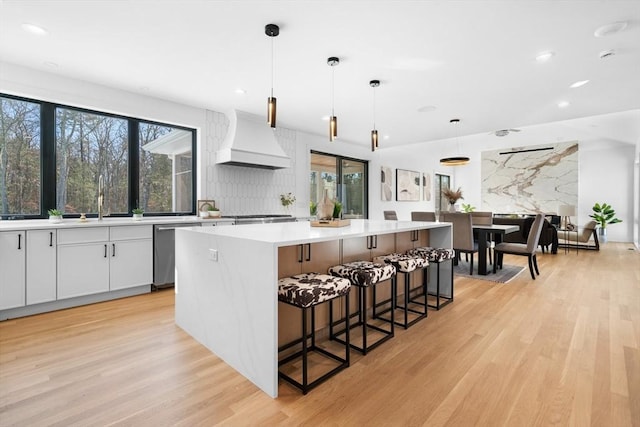 kitchen featuring a center island, stainless steel dishwasher, custom range hood, pendant lighting, and white cabinets