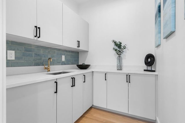 kitchen featuring sink, white cabinets, backsplash, and light wood-type flooring