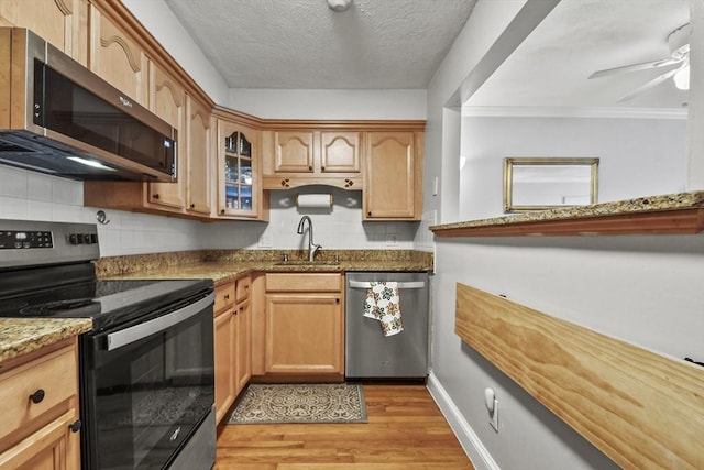 kitchen with light wood-style flooring, stainless steel appliances, a sink, light stone countertops, and glass insert cabinets