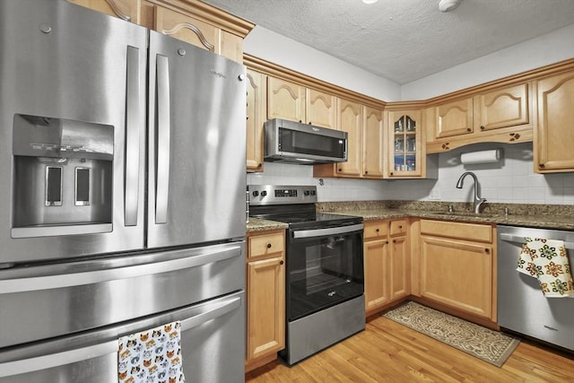 kitchen with light wood finished floors, dark stone counters, glass insert cabinets, stainless steel appliances, and a sink