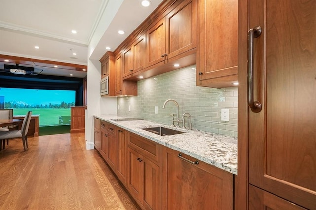 kitchen with light stone counters, brown cabinetry, light wood-style flooring, a sink, and stainless steel microwave