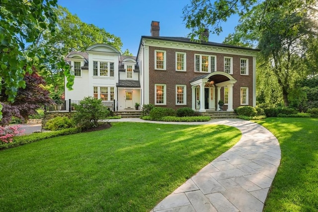 colonial inspired home with brick siding, a front yard, and a chimney