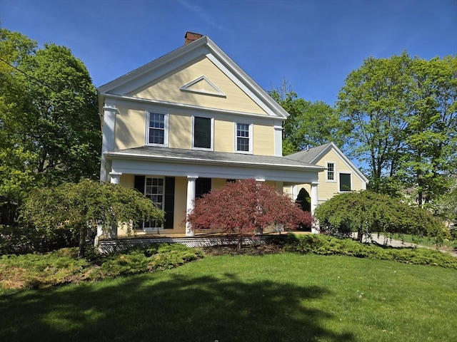 greek revival house featuring a porch, a chimney, and a front yard
