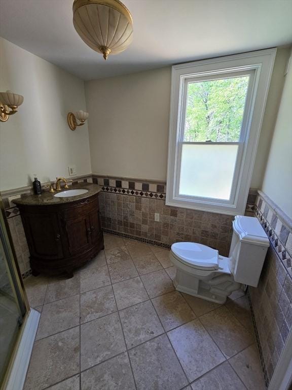 bathroom featuring toilet, tile patterned floors, tile walls, and a wainscoted wall