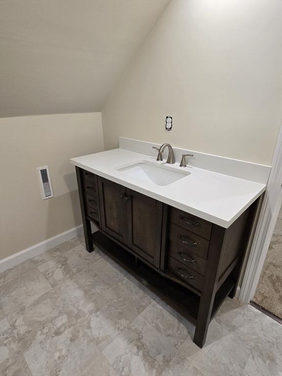 bathroom with baseboards, vaulted ceiling, visible vents, and vanity
