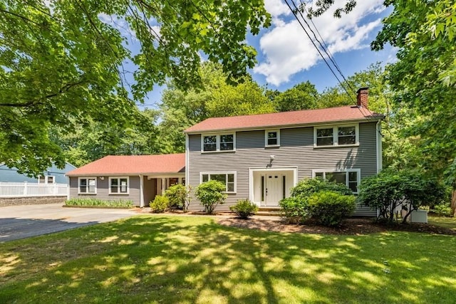 colonial inspired home featuring a front yard, fence, and a chimney