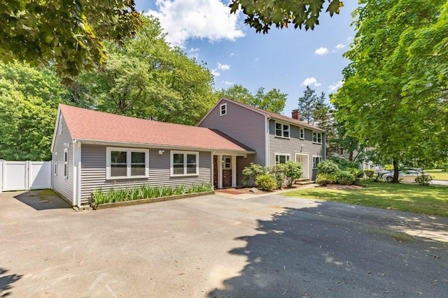 colonial home with a chimney, driveway, and fence