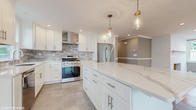 kitchen with appliances with stainless steel finishes, hanging light fixtures, a center island, white cabinetry, and wall chimney range hood