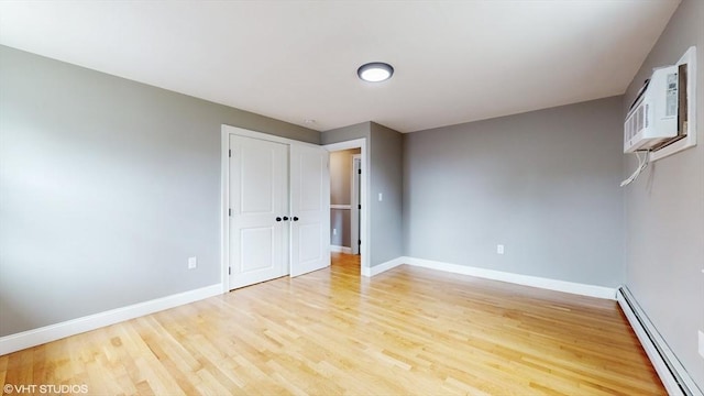 unfurnished bedroom featuring an AC wall unit, a baseboard heating unit, and light wood-type flooring