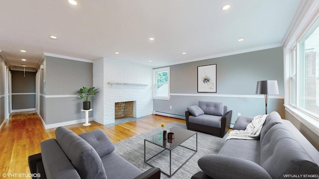 living room featuring a fireplace, baseboard heating, a wealth of natural light, and light wood-type flooring