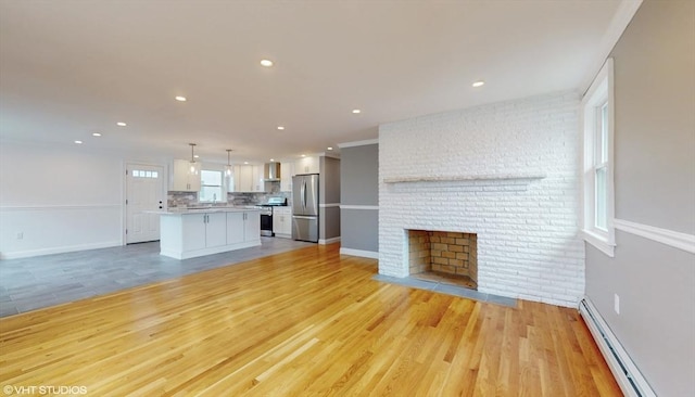 unfurnished living room with a brick fireplace, a baseboard heating unit, light hardwood / wood-style floors, and plenty of natural light