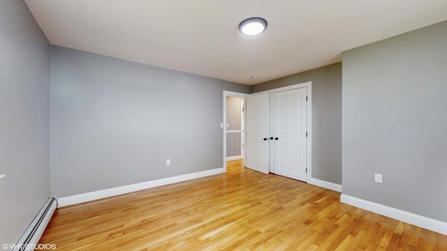 unfurnished bedroom featuring baseboard heating, light wood-type flooring, and a closet