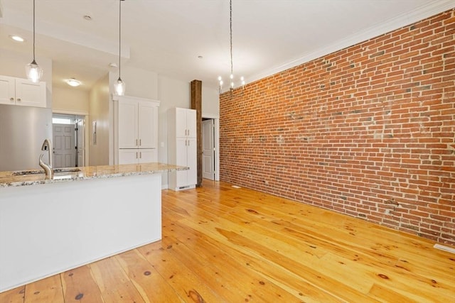 kitchen featuring light wood finished floors, hanging light fixtures, brick wall, and white cabinetry