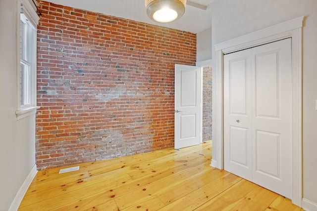 unfurnished bedroom with a closet, brick wall, baseboards, and light wood-style floors