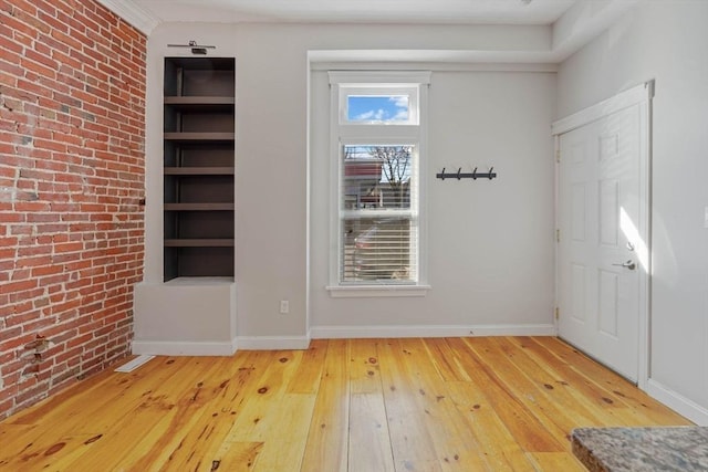 foyer with brick wall, light wood-type flooring, and baseboards