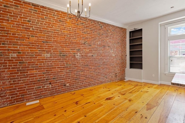 unfurnished dining area with visible vents, light wood-style flooring, ornamental molding, an inviting chandelier, and brick wall