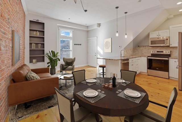 dining room featuring light wood-style flooring, brick wall, and baseboards