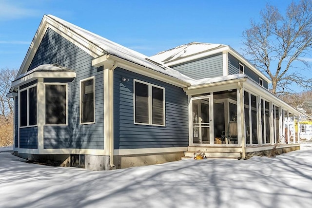 snow covered rear of property featuring a sunroom