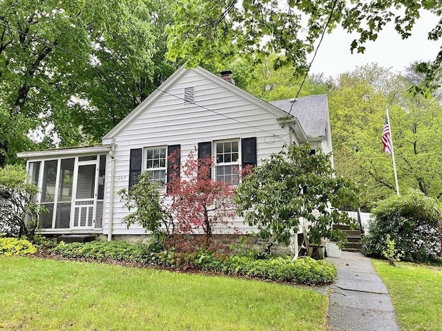 view of front of property featuring a sunroom, a chimney, and a front yard