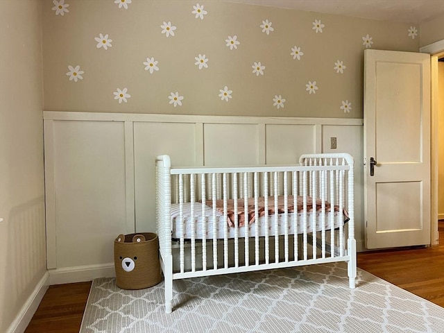 bedroom featuring a decorative wall, wood finished floors, wainscoting, a closet, and wallpapered walls