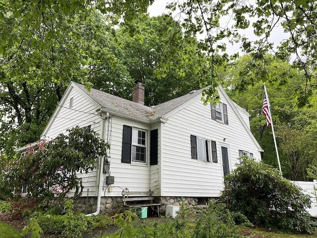view of side of home featuring a chimney and view of wooded area