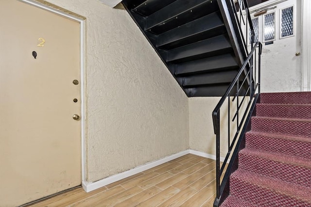 stairway featuring baseboards, a textured wall, and wood tiled floor