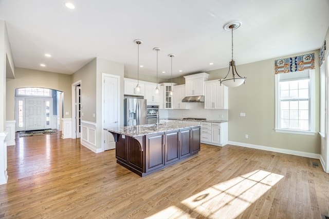 kitchen with a kitchen bar, stainless steel appliances, a center island with sink, white cabinetry, and light wood-type flooring