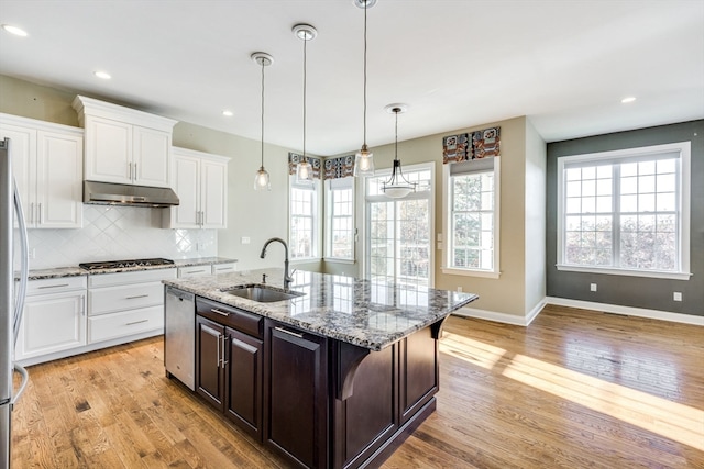 kitchen with light hardwood / wood-style floors, a kitchen island with sink, a breakfast bar, light stone countertops, and white cabinetry