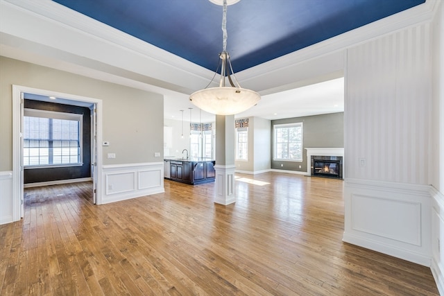 unfurnished dining area featuring hardwood / wood-style flooring, sink, a raised ceiling, and decorative columns