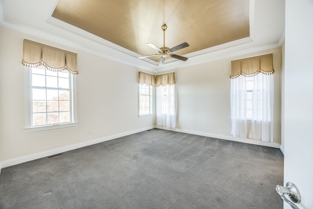 empty room with ceiling fan, plenty of natural light, dark carpet, and a tray ceiling