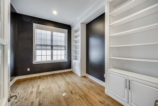 spare room featuring light hardwood / wood-style flooring, crown molding, and built in features