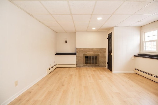 unfurnished living room featuring a drop ceiling, a baseboard heating unit, a stone fireplace, and light wood-type flooring