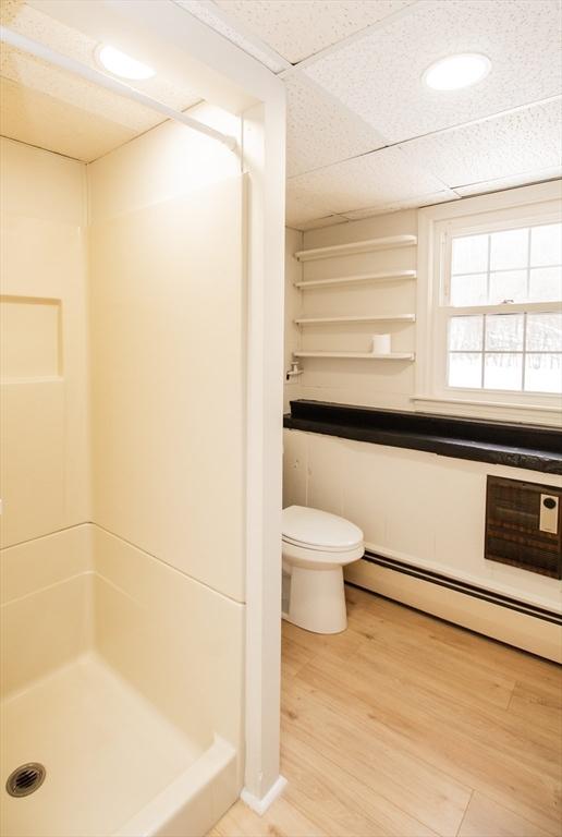 bathroom with a baseboard radiator, a shower, hardwood / wood-style flooring, toilet, and a drop ceiling